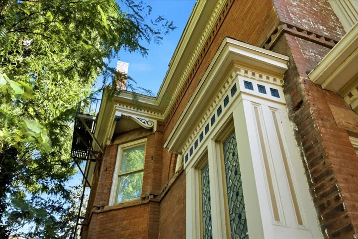 Brick exterior with ornate white trim, leaded glass window, and decorative corbels