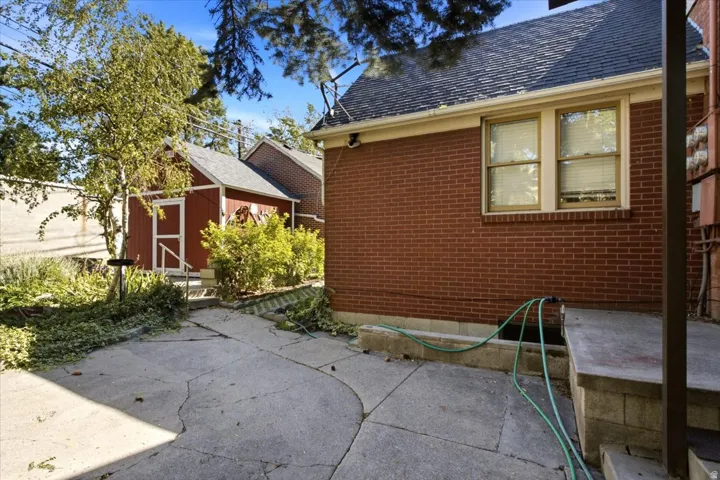 Brick exterior with two windows, concrete patio, and separate storage shed