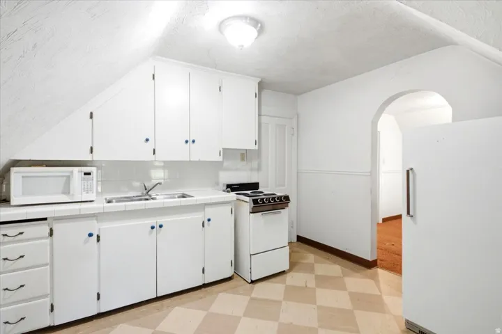 Kitchen featuring white cabinetry, tile backsplash, double basin sink, and checkered flooring