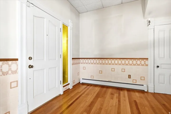 Hardwood flooring, white panel door, decorative wall tiling, and a textured glass sidelight