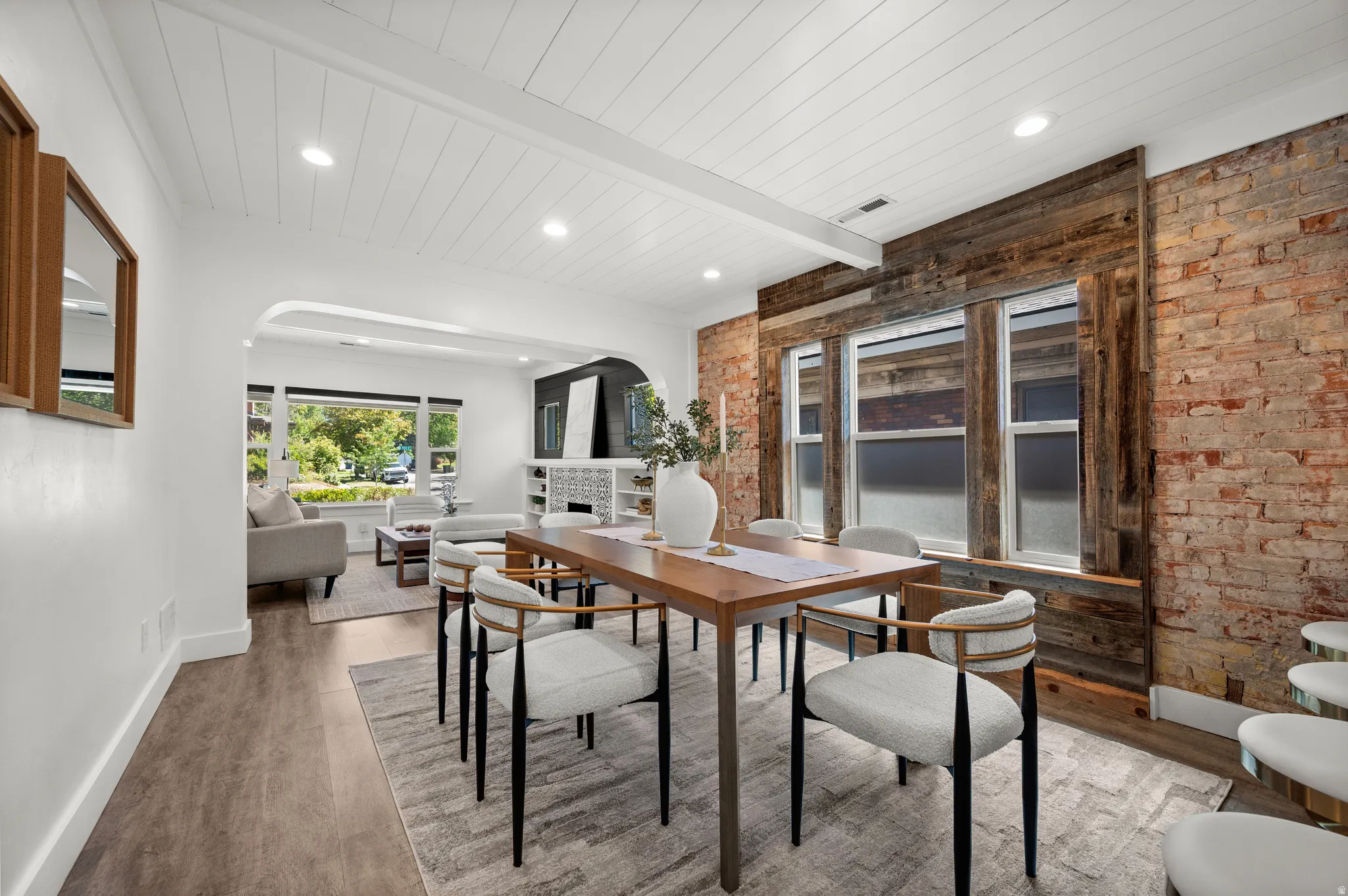 Wood-finish flooring throughout, white shiplap ceiling, exposed brick accent wall, and three paneled windows