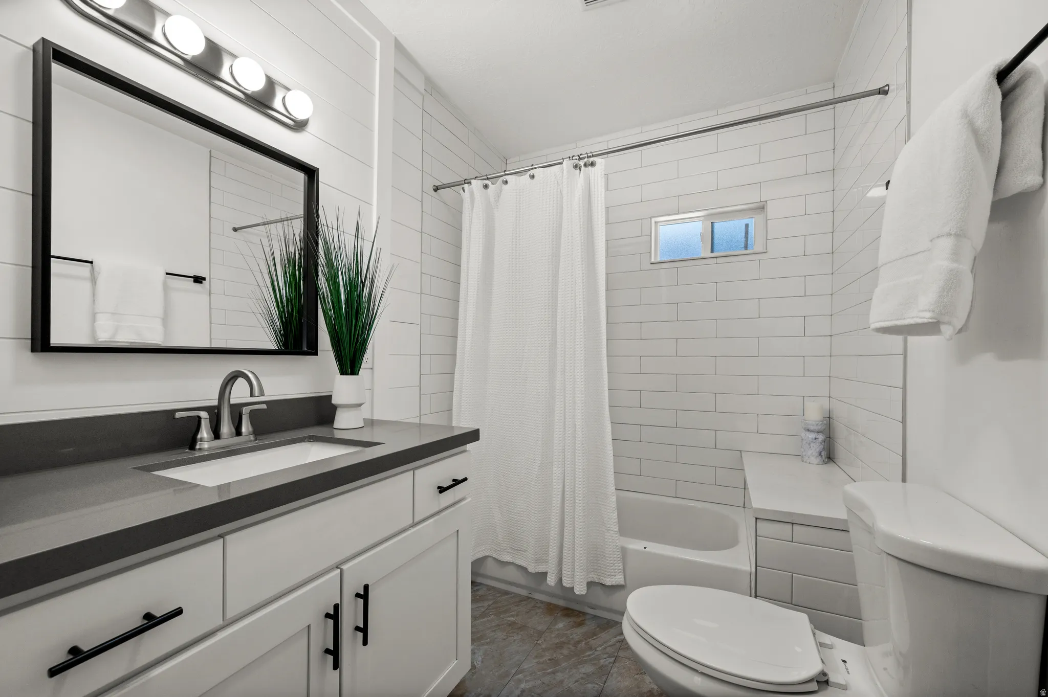 White subway tile shower surround with integrated shelving, vanity with a dark countertop and undermount sink, brushed nickel faucet, and wood-finish flooring