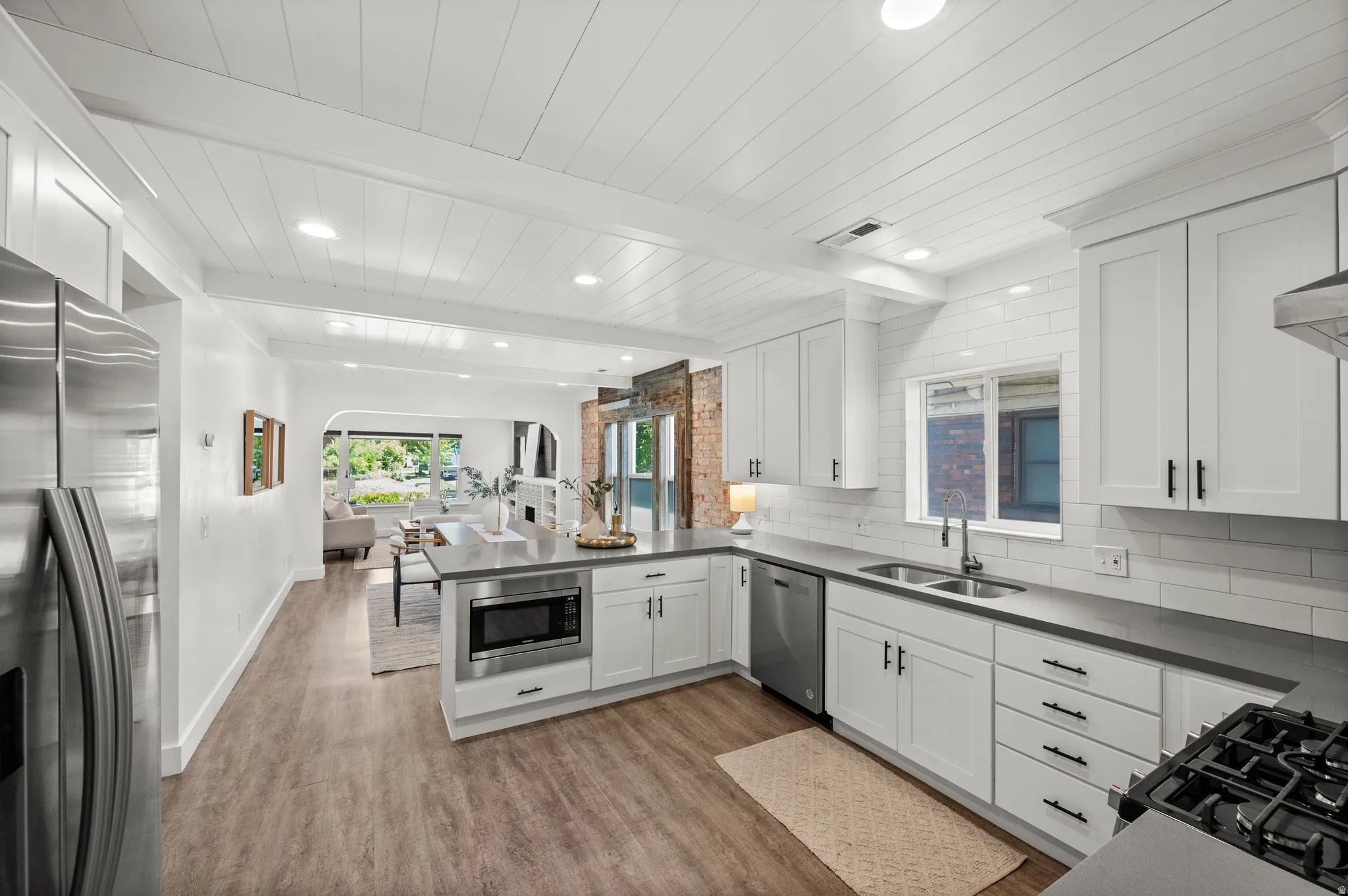 Kitchen featuring white shaker-style cabinetry, stainless steel appliances, dark countertops, white subway tile backsplash, and wood-finish flooring