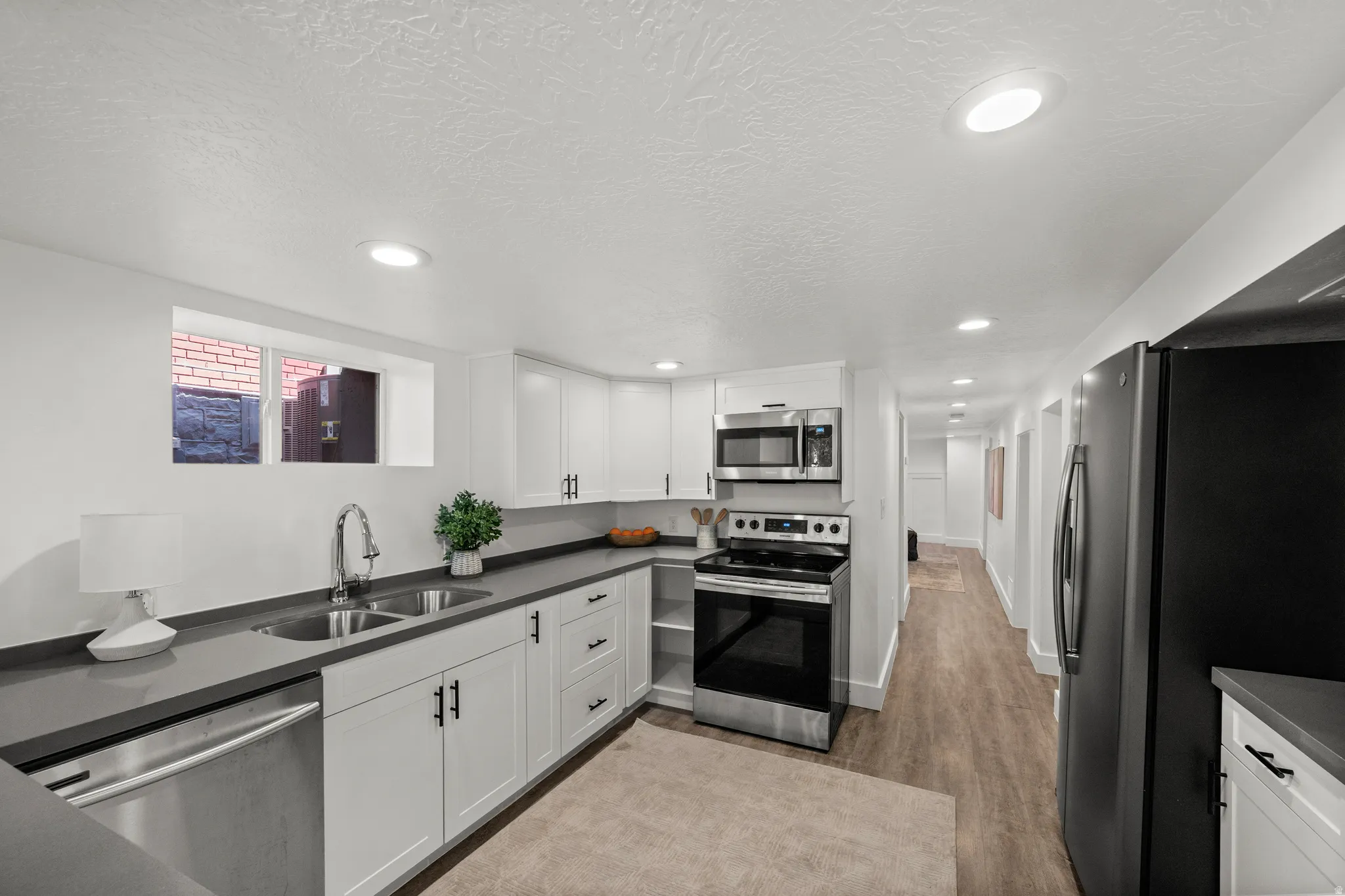 Modern kitchen featuring white cabinetry, dark countertops, stainless steel appliances, and wood-finish flooring