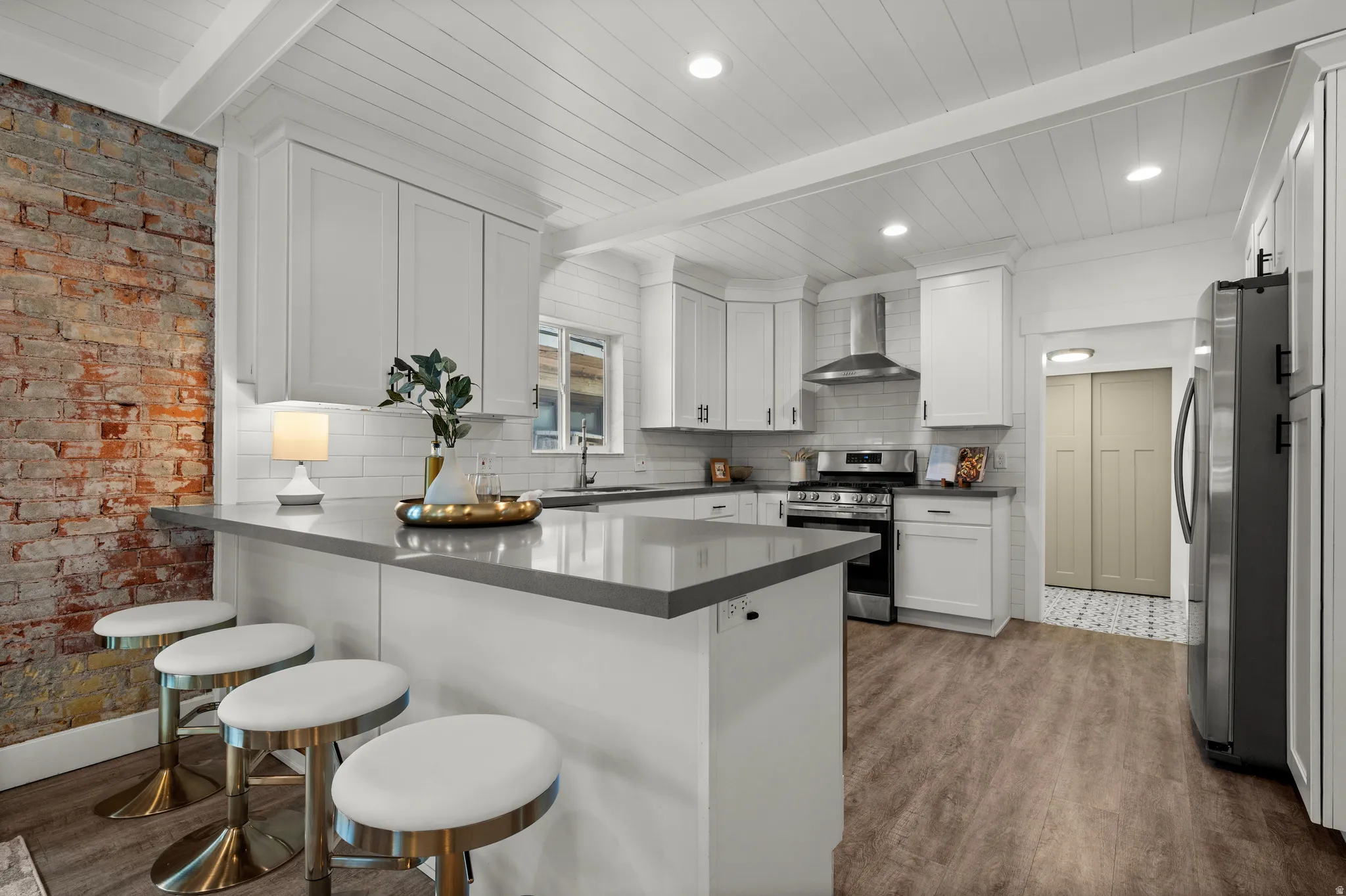 Spacious kitchen featuring an exposed brick accent wall, wood-finish flooring, white shaker cabinets, and recessed lighting