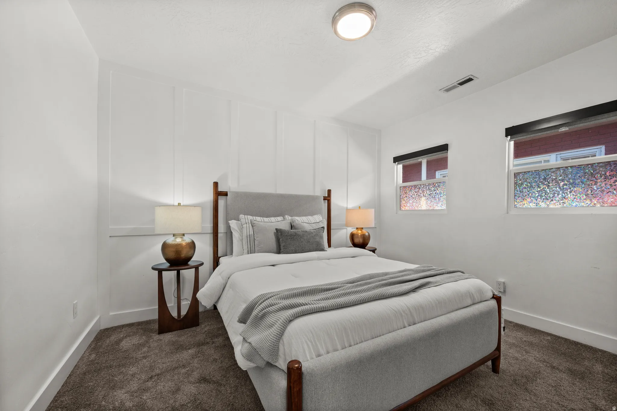 White walls with accent paneling, carpeted flooring, and two windows with roller shades