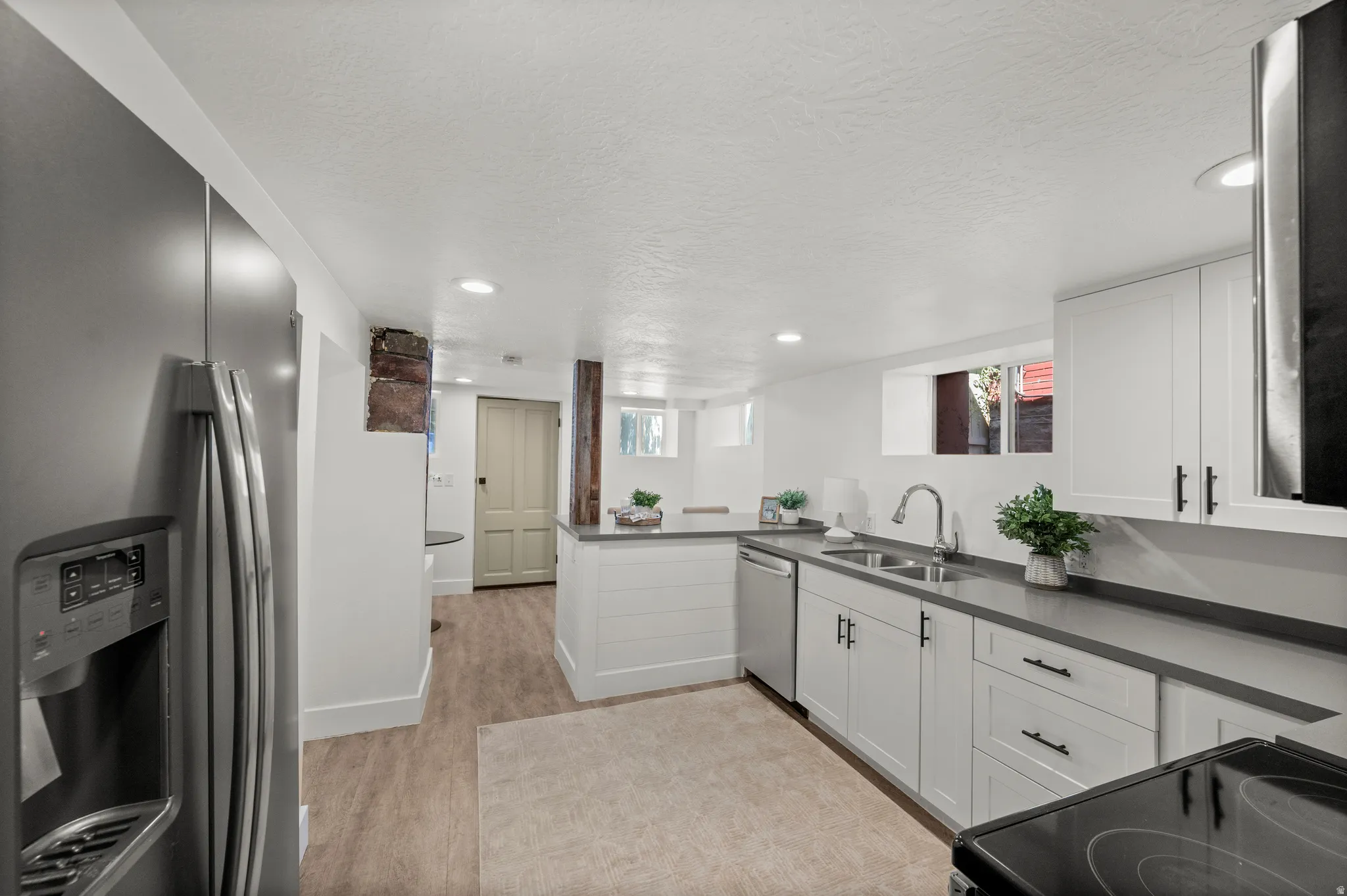Kitchen featuring wood-finish flooring, white cabinetry with dark hardware, stainless steel appliances, dark countertops, and recessed lighting