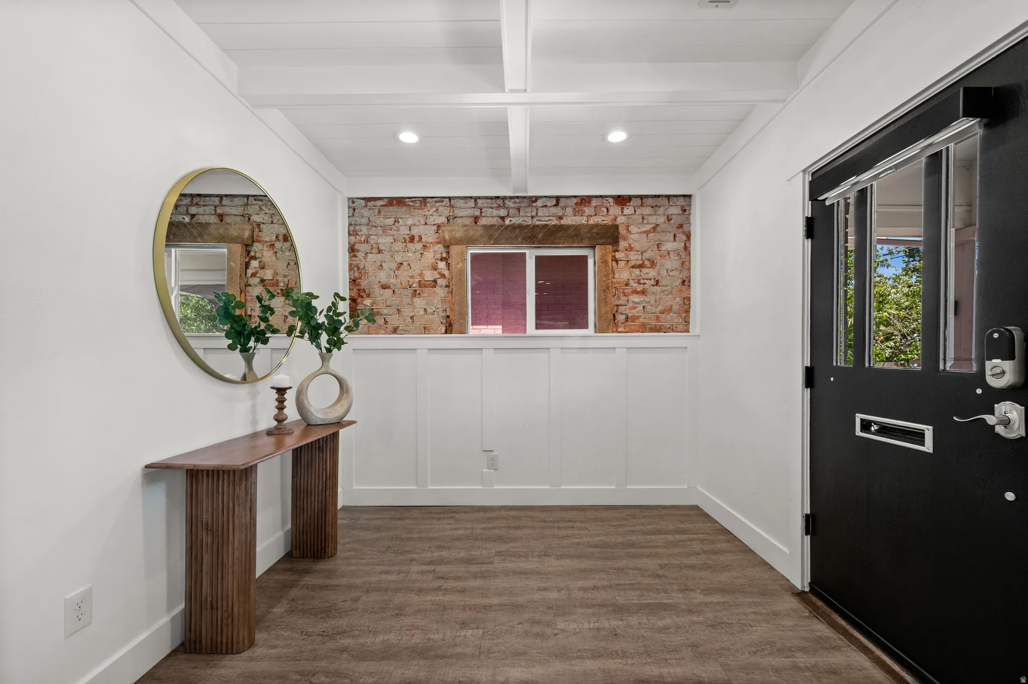 Exposed brick wall feature, white wainscoting, wood-finish flooring, recessed lighting, and a black entry door with transom windows