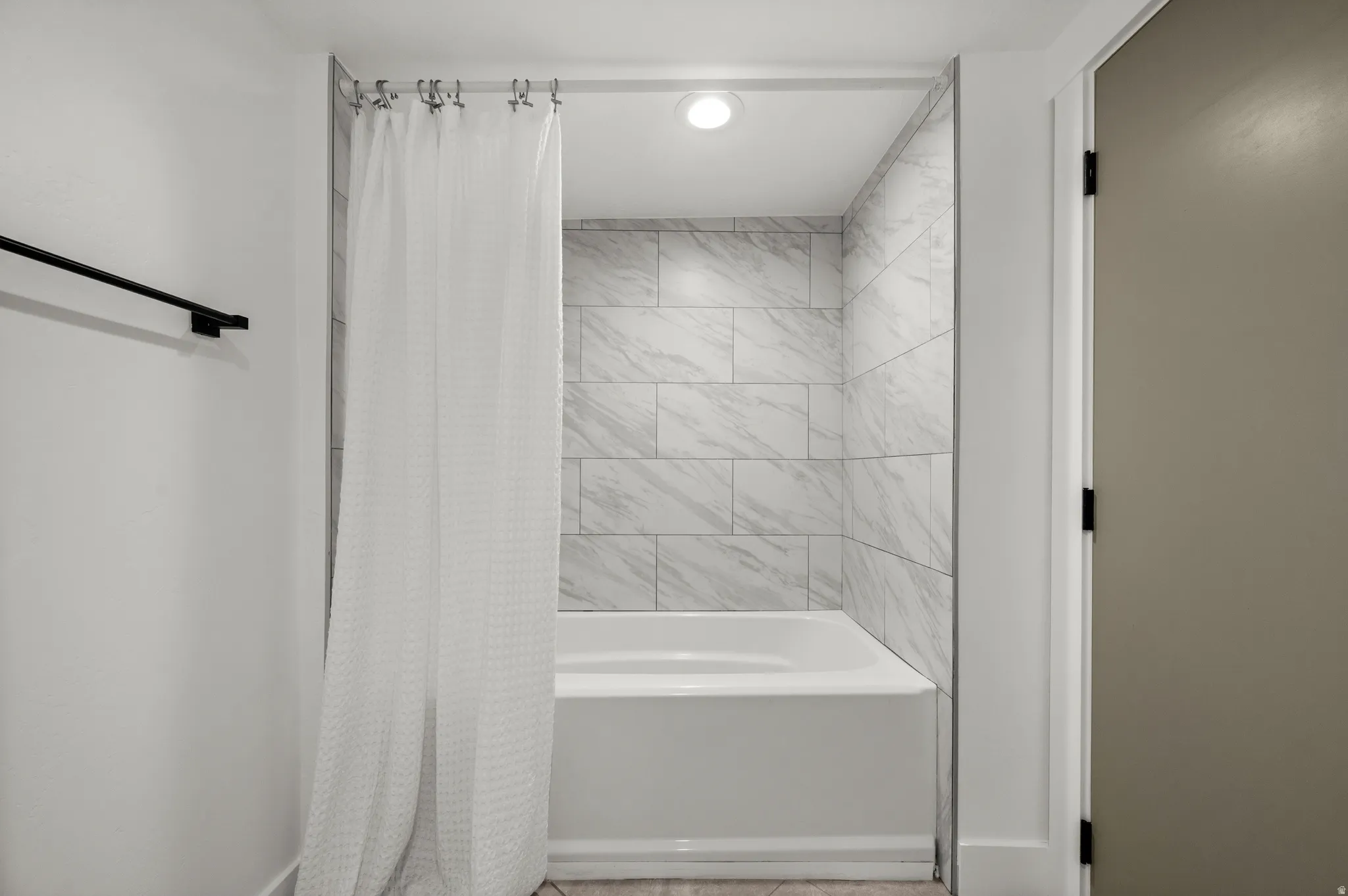 Recessed lighting illuminates the bathtub with subway tile surround and a matte black towel bar