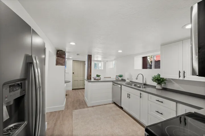 Kitchen featuring wood-finish flooring, white cabinetry with dark hardware, stainless steel appliances, dark countertops, and recessed lighting