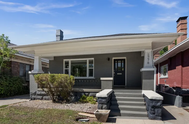 Covered front porch with substantial pillars, stone-clad porch steps, a dark gray entry door with window panes, and horizontal siding