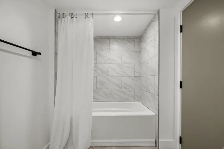 Recessed lighting illuminates the bathtub with subway tile surround and a matte black towel bar