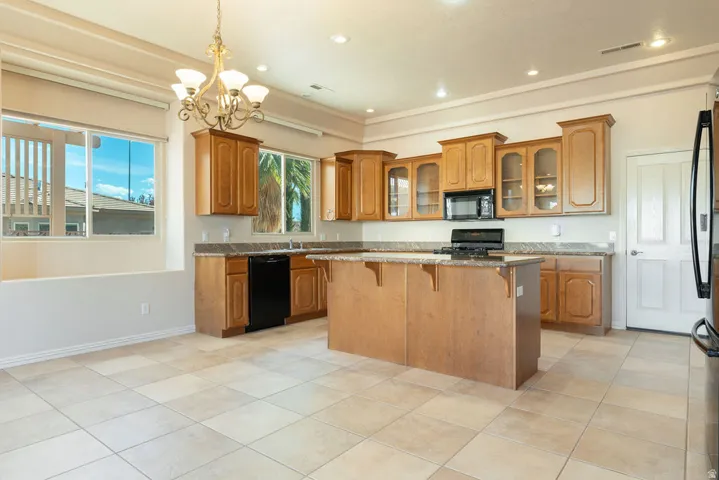 Kitchen featuring wood cabinetry, a central island, dark-toned appliances, and tiled flooring