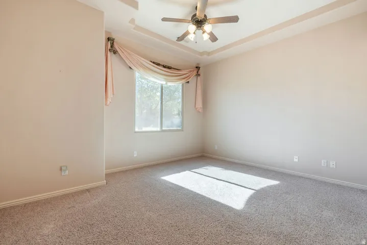 Tray ceiling with ceiling fan, large window, and carpet flooring