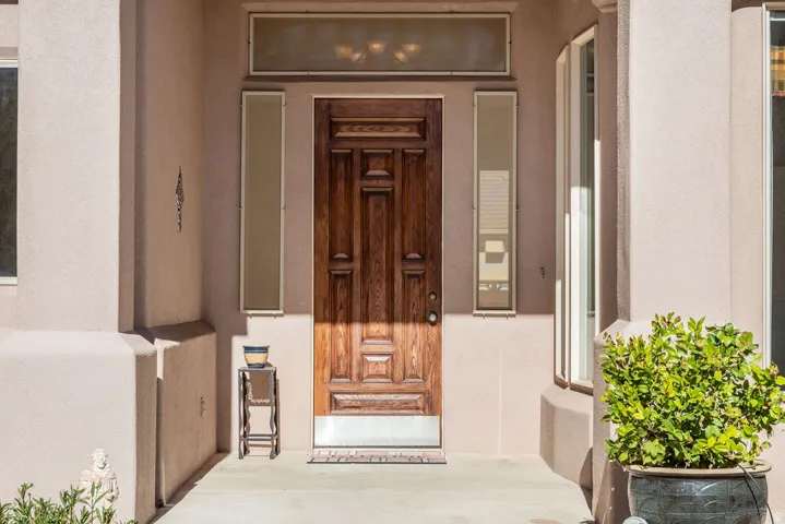 Wood-paneled entry door with sidelights and transom window, stucco exterior, and concrete entryway