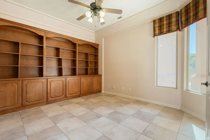 Built-in wood shelving and cabinetry, tiled flooring, ceiling fan, and multiple windows