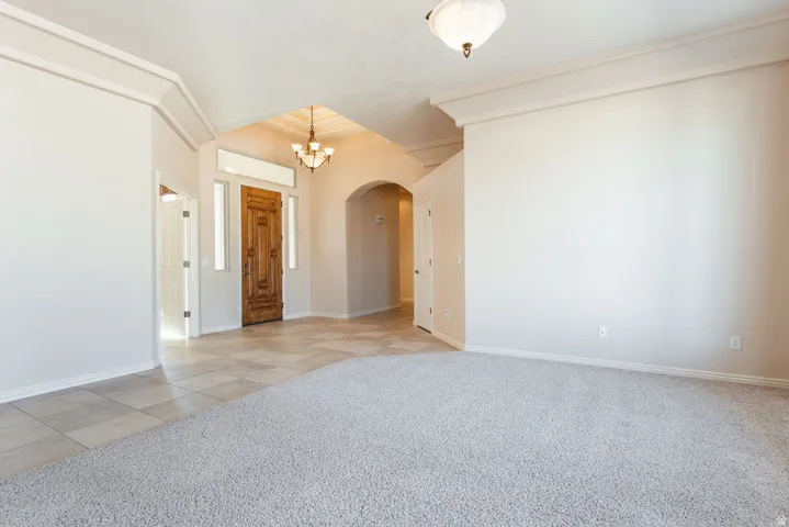 Spacious interior featuring a carved wood entry door, tile flooring, recessed arched doorways, and a chandelier lighting fixture