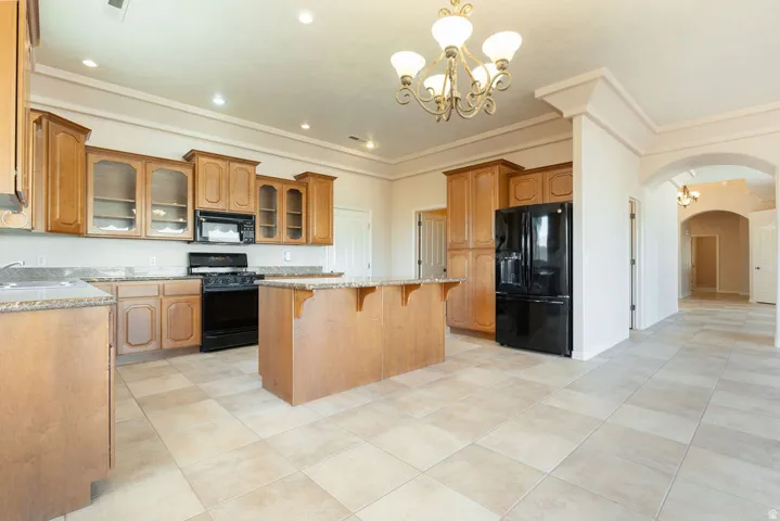 Kitchen featuring wood cabinetry, stone-finish countertops, black appliances, a central island, and tile flooring