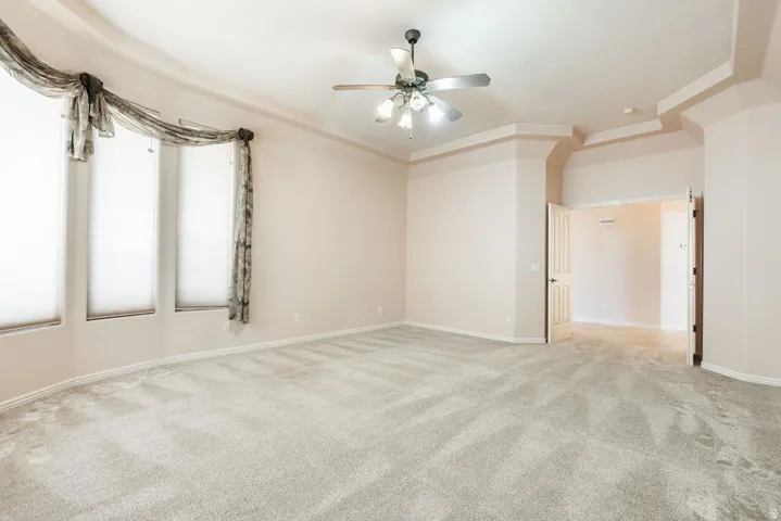 Recessed ceiling, ceiling fan with light fixture, light-toned carpeting, multiple windows, and paneled doors