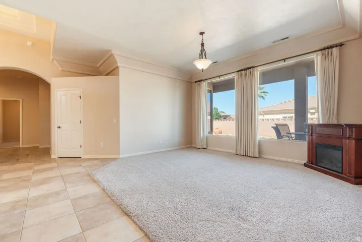 Recessed ceiling with layered trim, tiled flooring, arched doorway, and built-in decorative fireplace