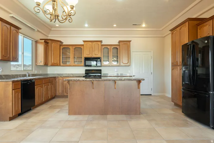 Kitchen featuring wood-finish cabinetry, a central island, black appliances, tile flooring, and a decorative chandelier
