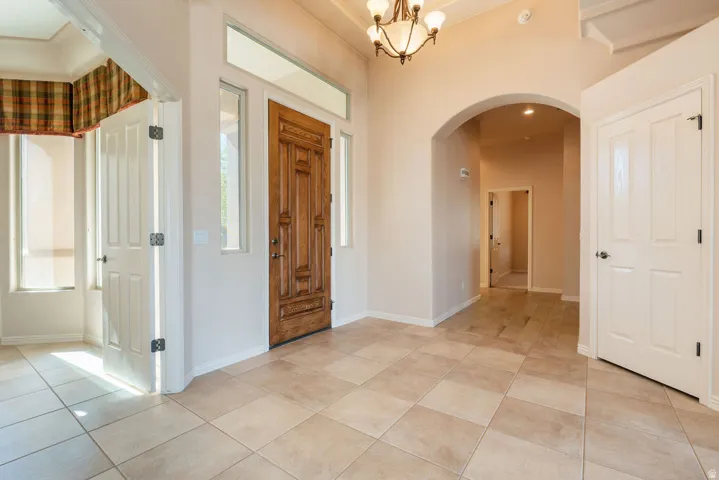 Entryway featuring tile flooring, an ornate wood-paneled door, arched doorway, and chandelier lighting