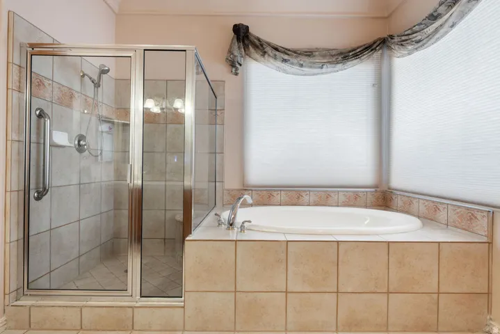 Tile-surrounded soaking tub, separate glass-enclosed shower with tile walls, and dual window treatments
