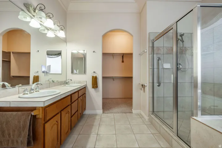 Double vanity with tile countertop, wood-finish cabinetry, and decorative lighting