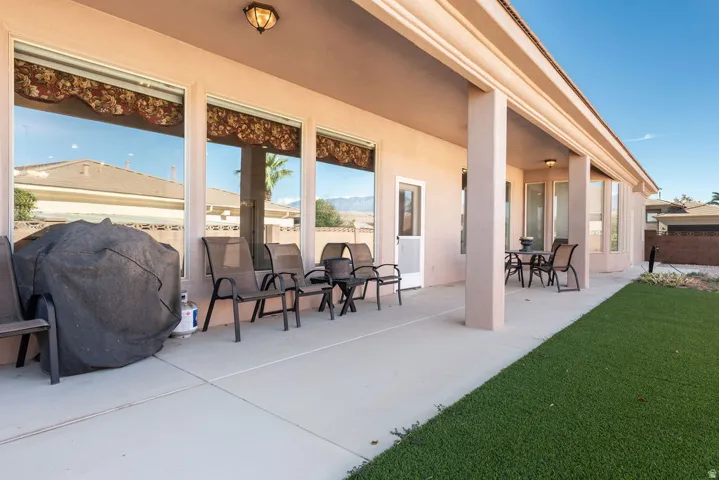 Expansive covered patio with concrete flooring, multiple large windows, and a turf lawn