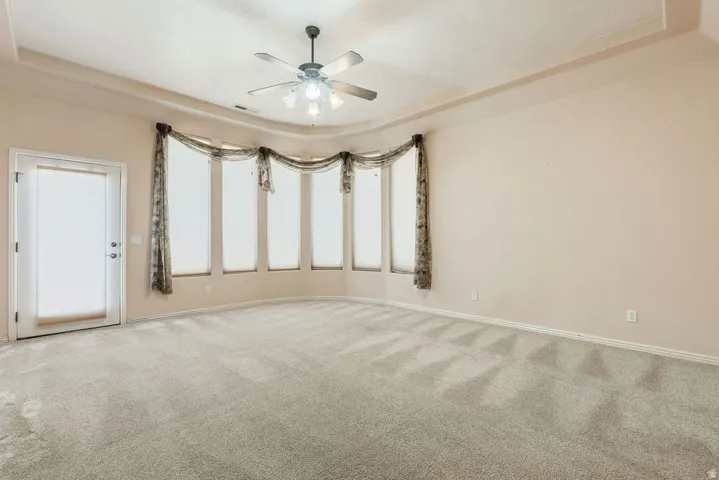 Bay window with multiple panels, ceiling fan with integrated lighting, tray ceiling, and neutral carpet flooring