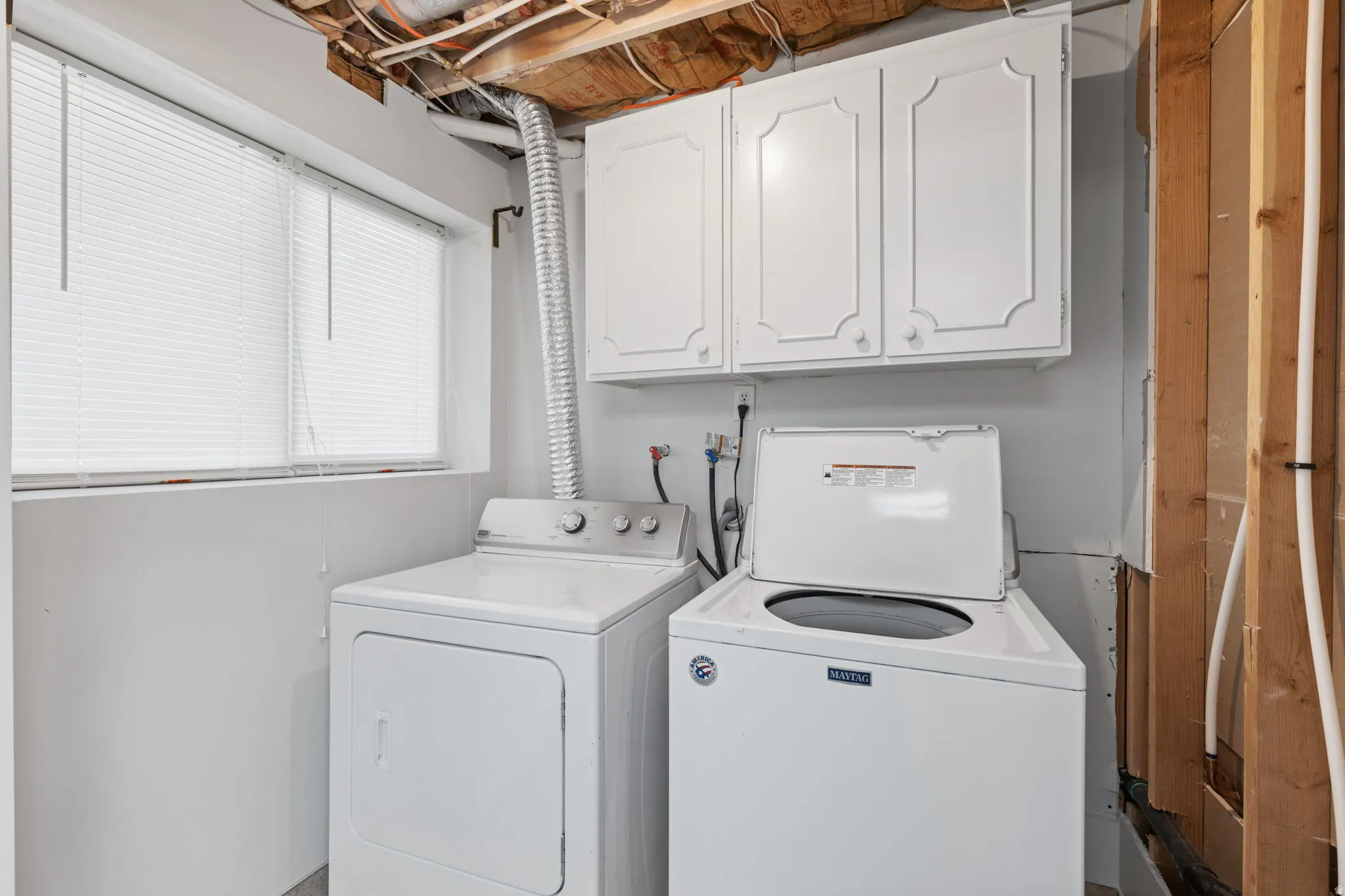White cabinetry, two windows with blinds, a washing machine, and a clothes dryer