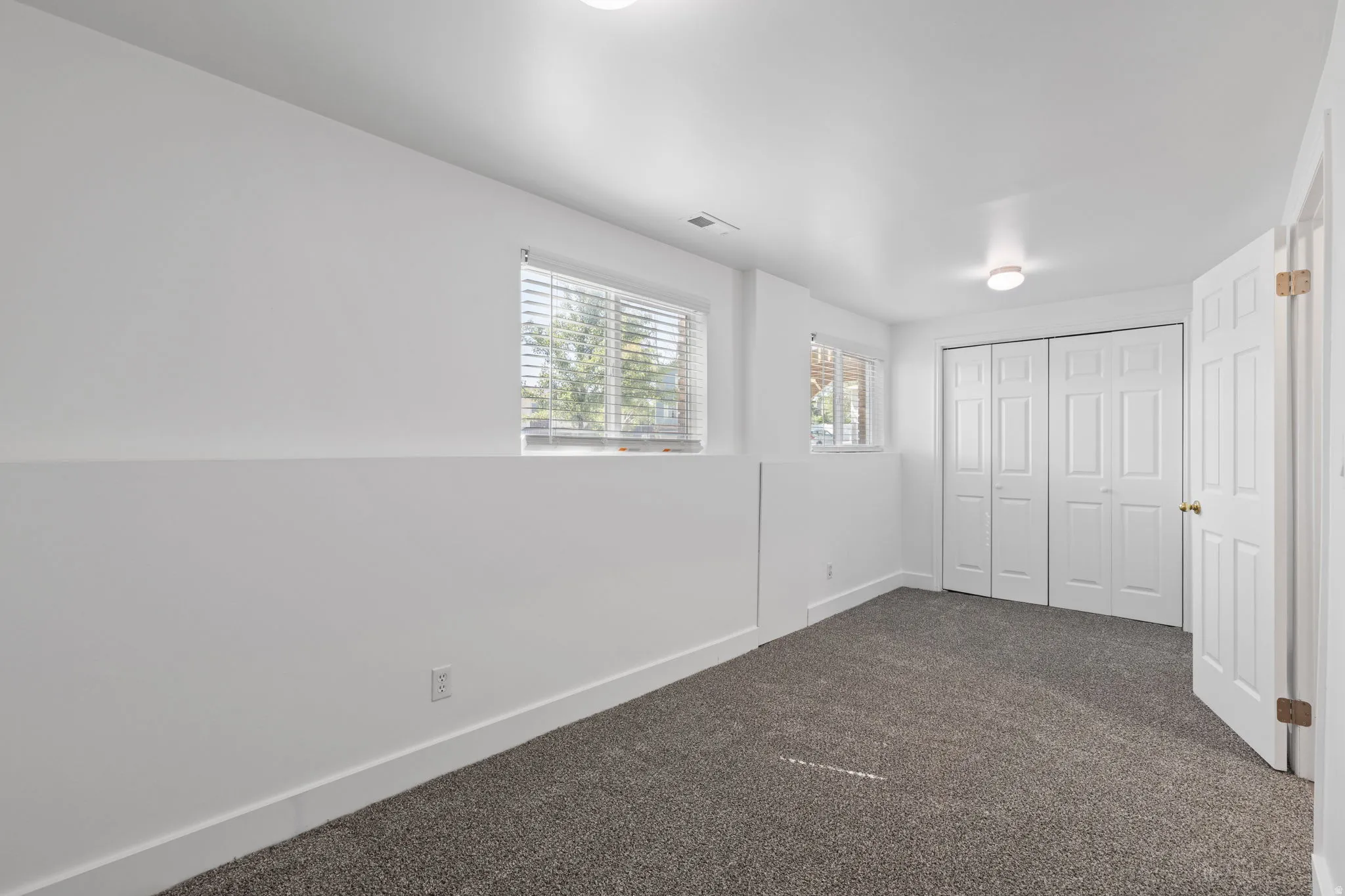 Plush carpet flooring, dual windows with blinds, recessed lighting, and white bi-fold closet doors
