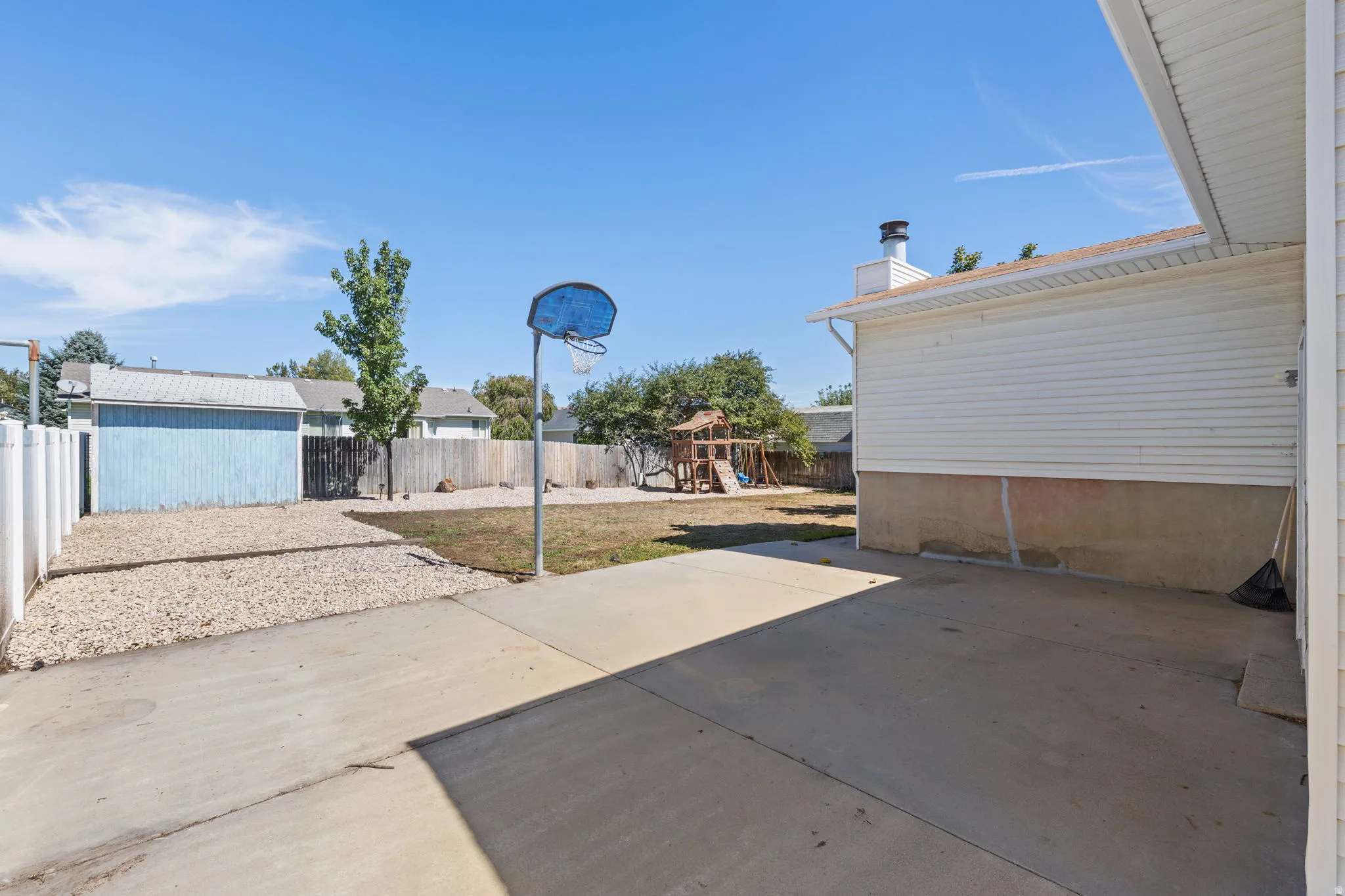 Expansive concrete patio with a basketball hoop, gravel area, fenced yard, and a detached storage shed