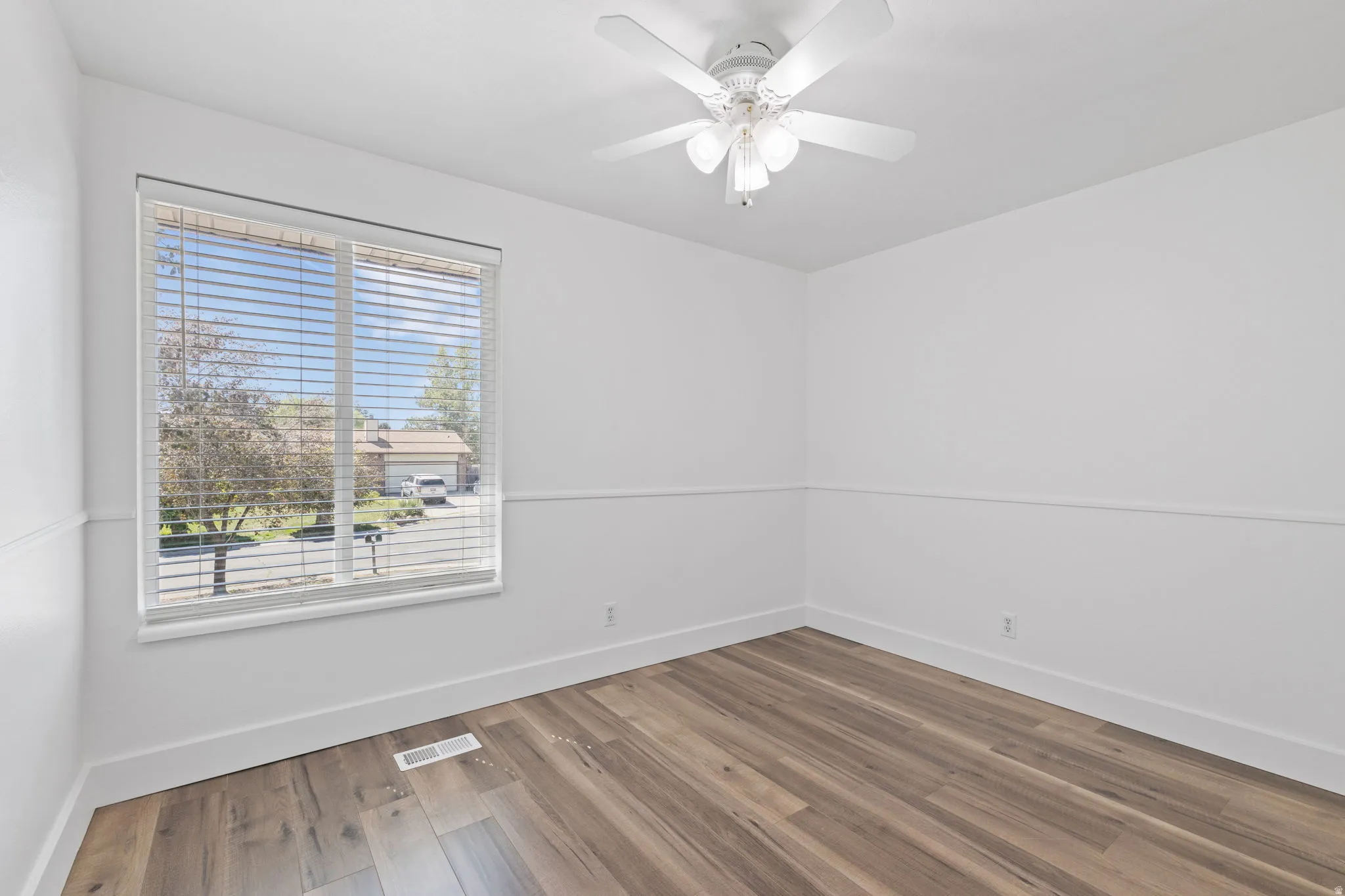 Spacious room featuring wood-finish flooring, white walls with decorative molding, and a ceiling fan