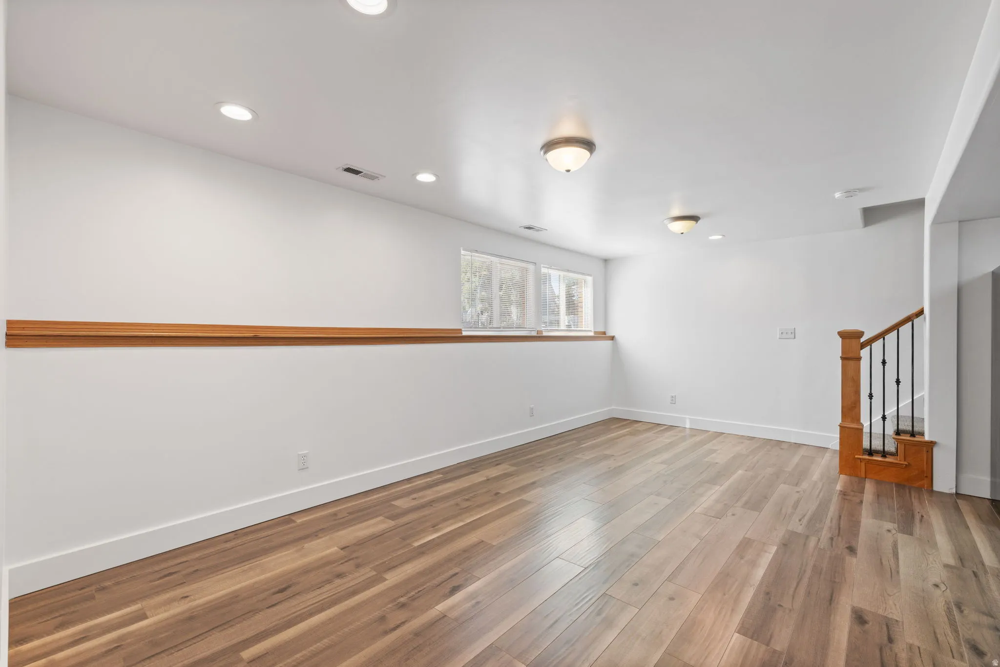 Wood-finish flooring, recessed lighting, double windows, wood trim, and a staircase with wrought iron balusters