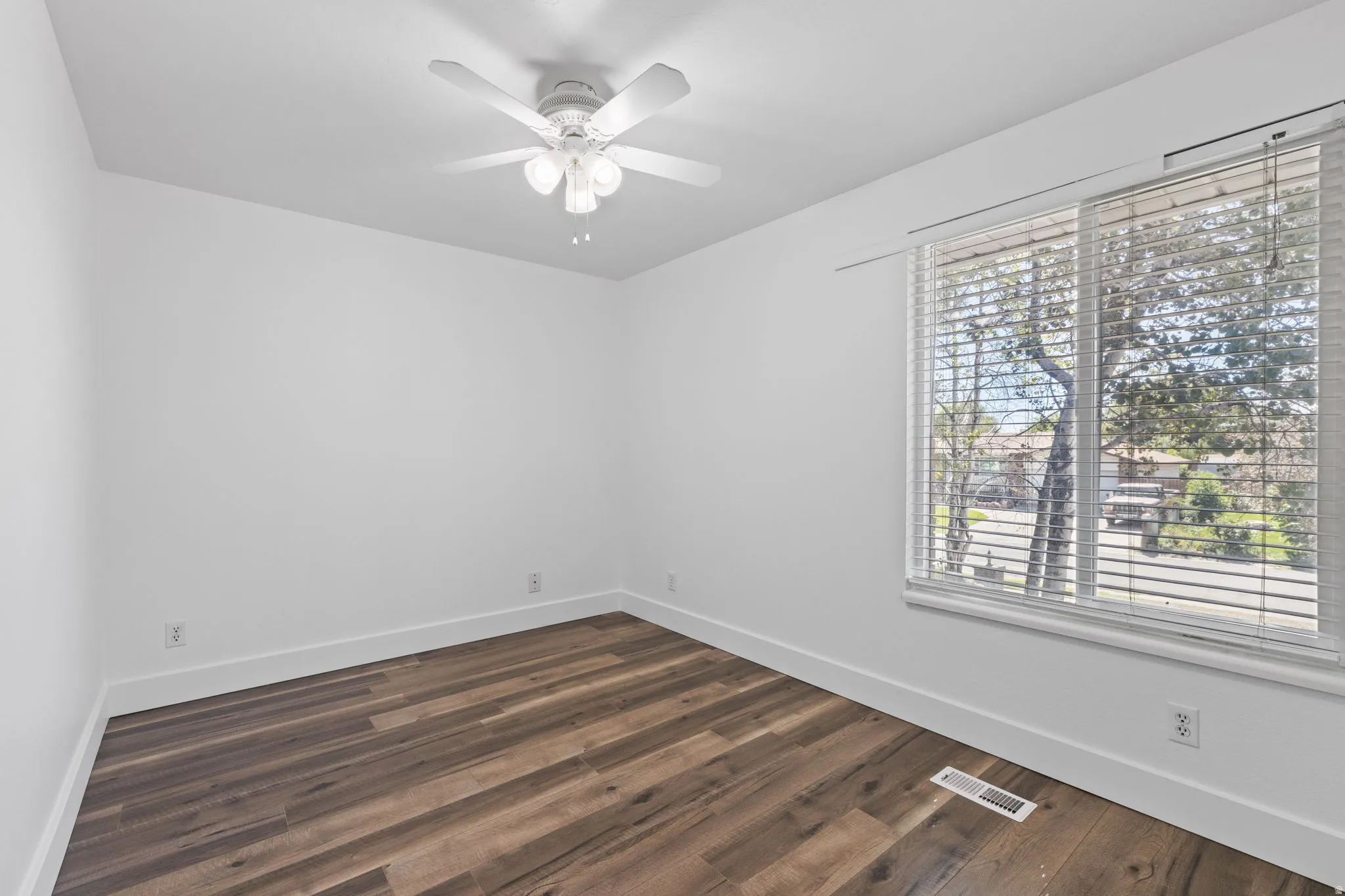 Wood-finish flooring, white walls, ceiling fan with integrated lighting, and a window with blinds