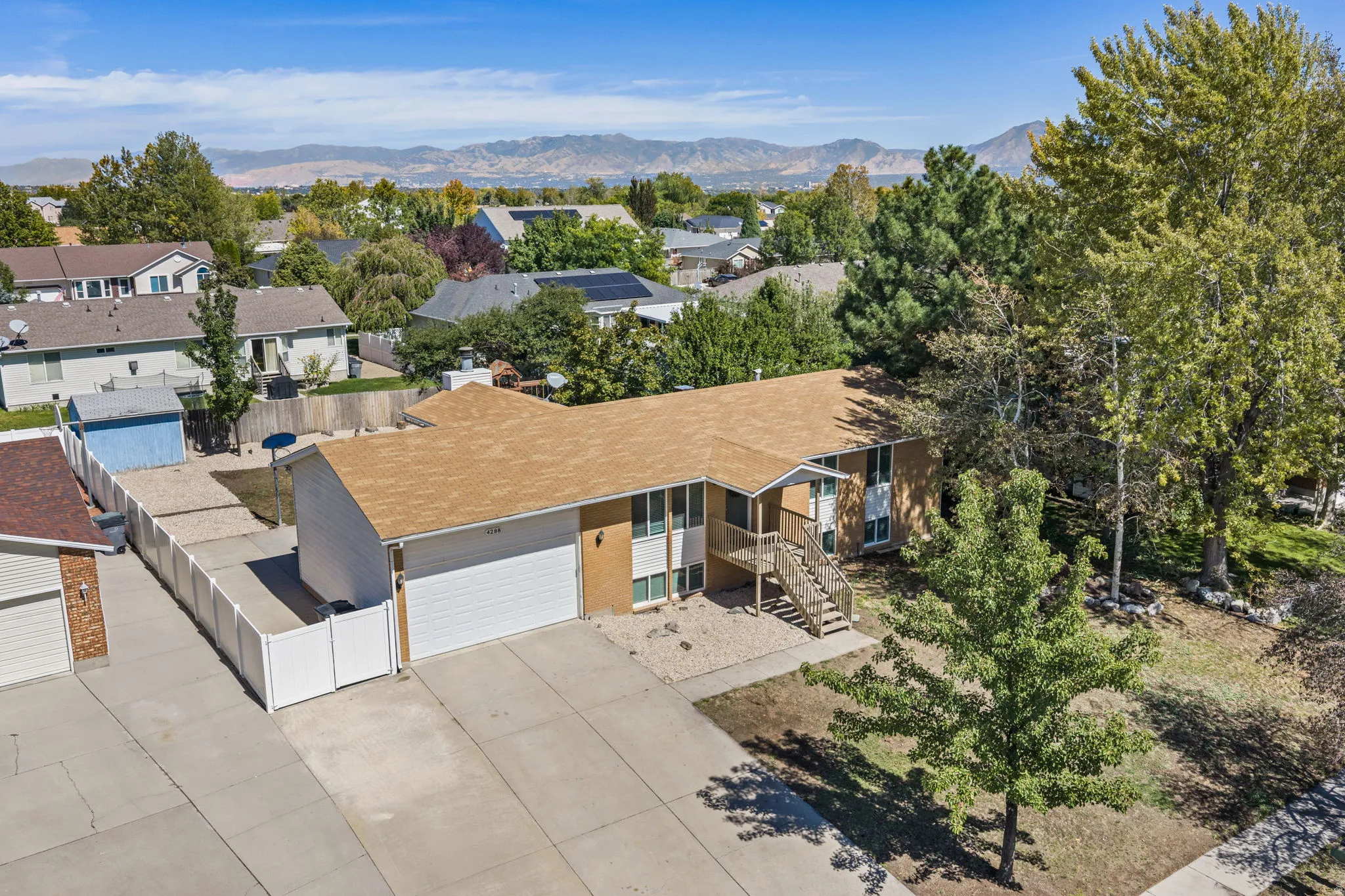 Split-level residence featuring an attached two-car garage, mature landscaping, and a fenced side yard