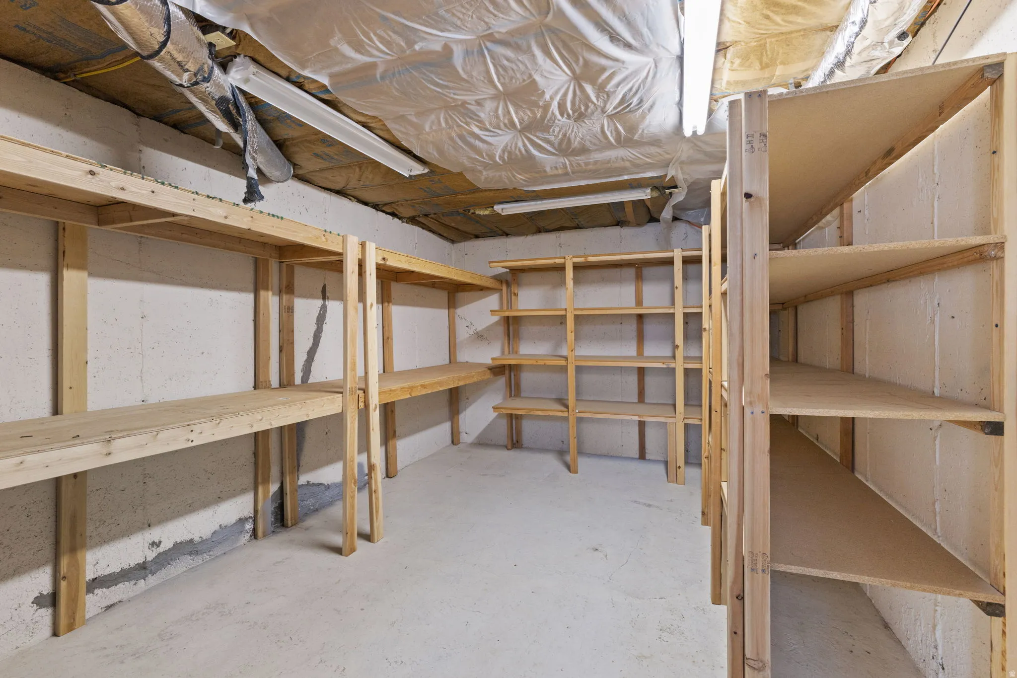 Basement storage area featuring extensive built-in wooden shelving, concrete floor, and exposed ceiling utilities