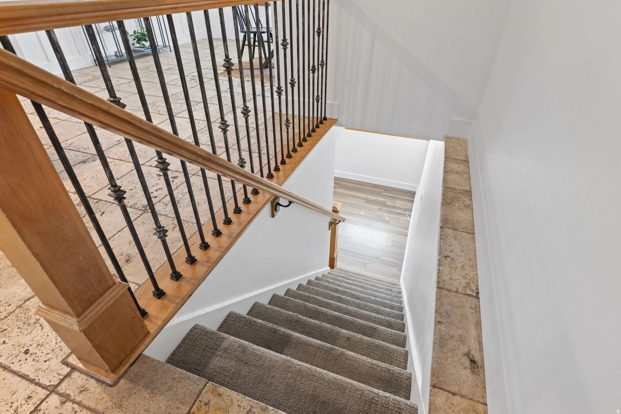 Hardwood railing with wrought iron balusters, stone-finish flooring, and carpeted stairs