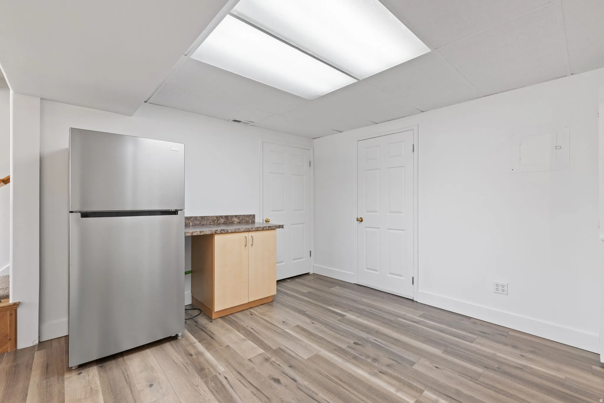 Stainless steel refrigerator, wood-finish flooring, light wood-toned cabinetry, speckled countertop, and recessed ceiling lighting