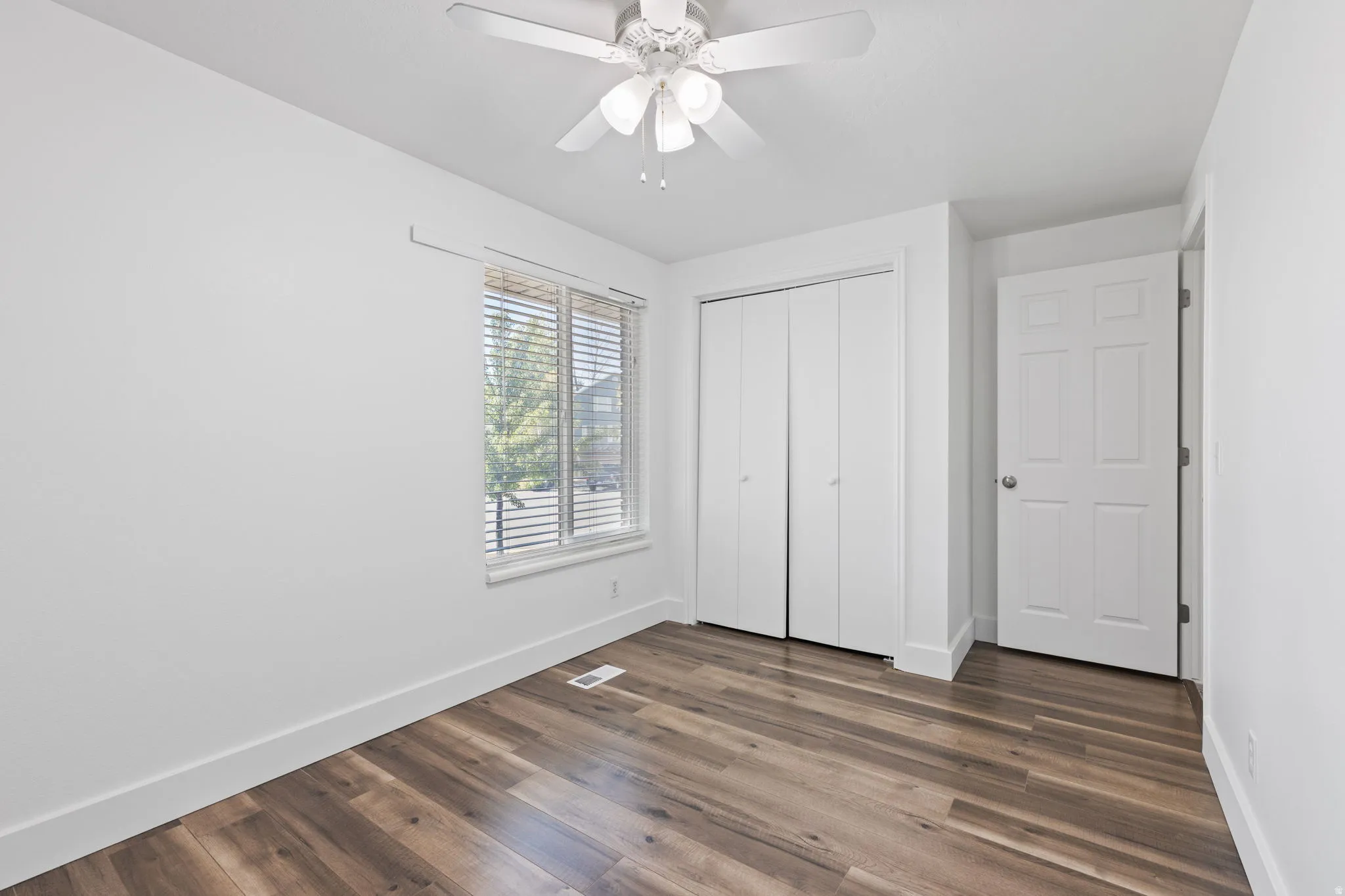 Wood-finish flooring, white walls, and a window with blinds