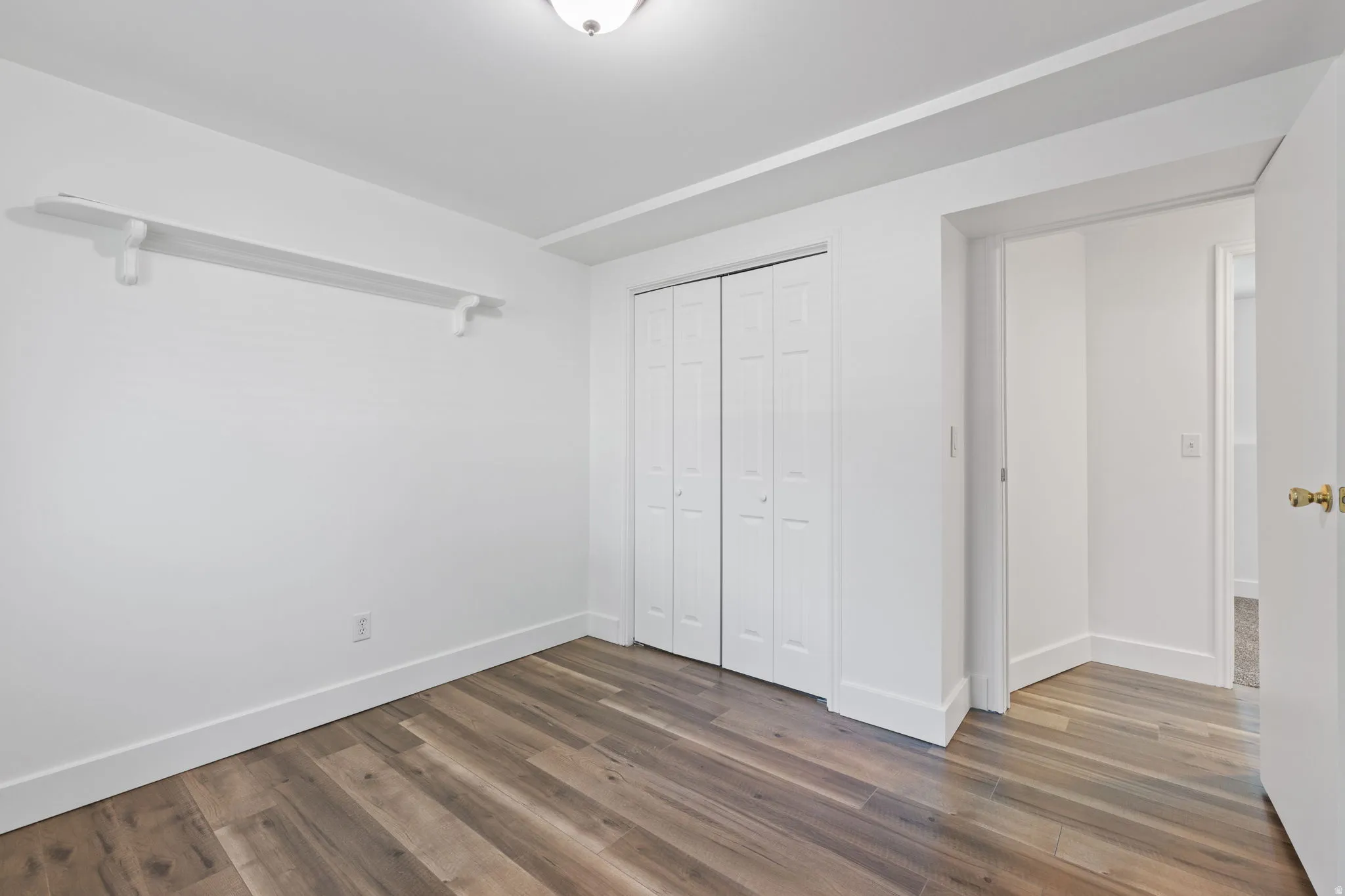 Wood-finish flooring, white bi-fold closet doors, white trim, and a white wall shelf