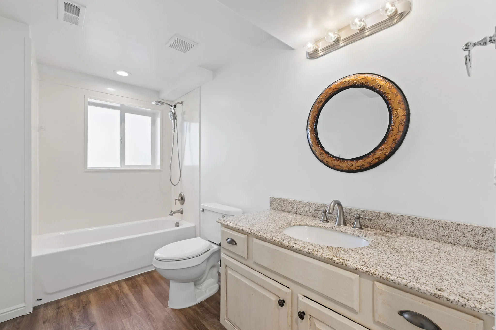 Wood-finish flooring, white vanity with light-toned countertop, integrated sink with brushed nickel faucet, and a white bathtub with shower fixture