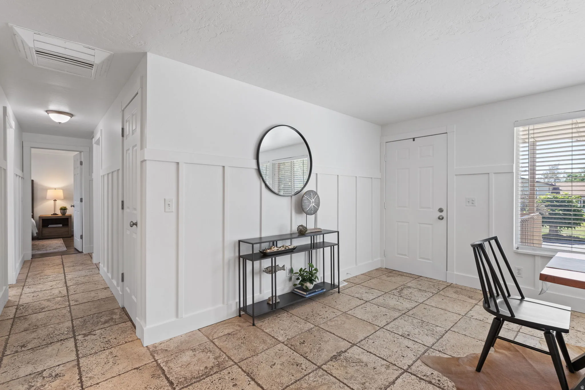 Tiled flooring extending throughout, crisp white board and batten wall detailing, a paneled entry door, and a single window with horizontal blinds