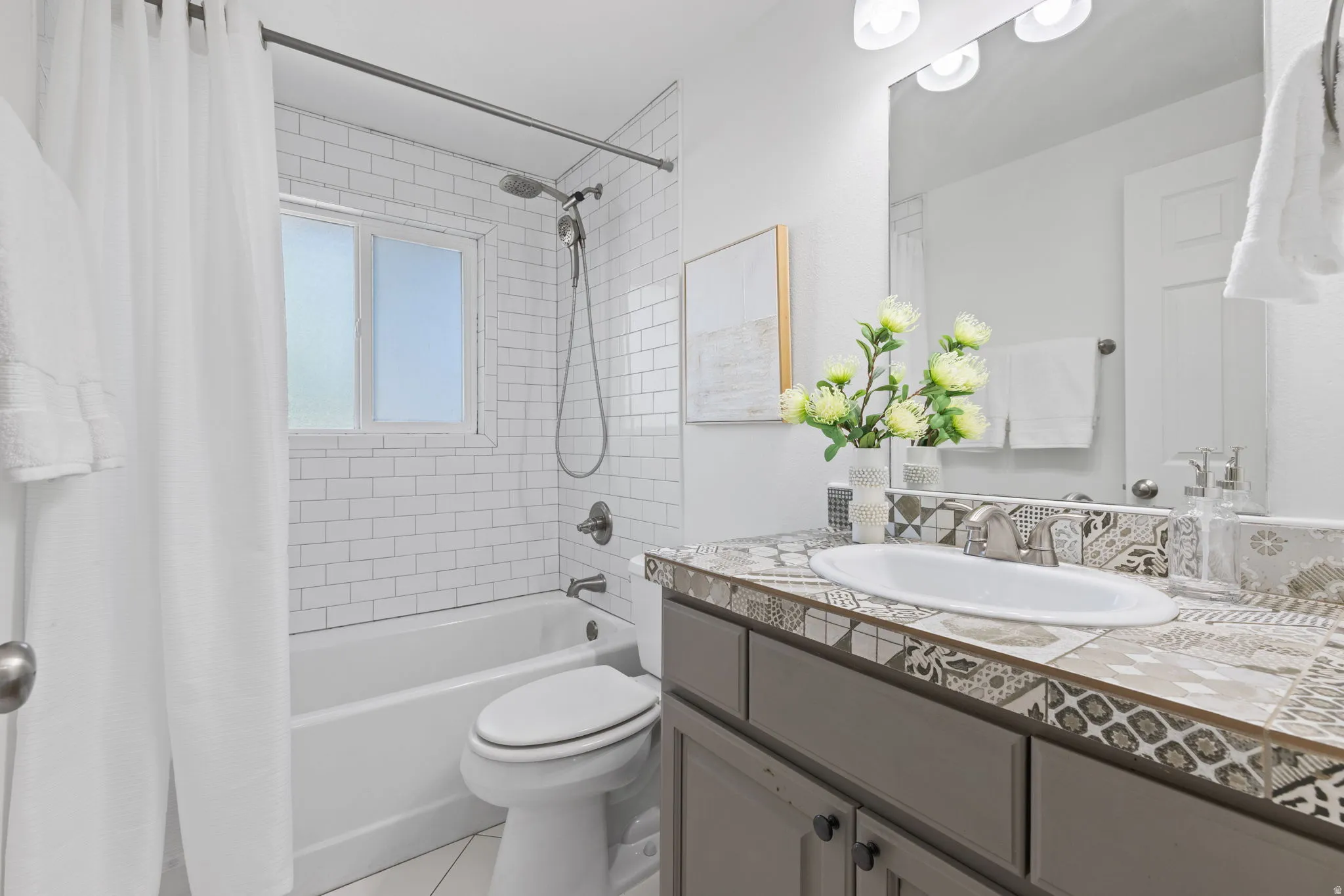 Subway tile bath surround with a window, a single vanity with a patterned tile countertop, and a built-in mirror with overhead lighting