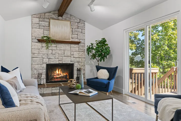Vaulted ceiling with exposed wood beam, stone-surround fireplace with wood mantel, light wood-finish flooring, and sliding glass door with outdoor access