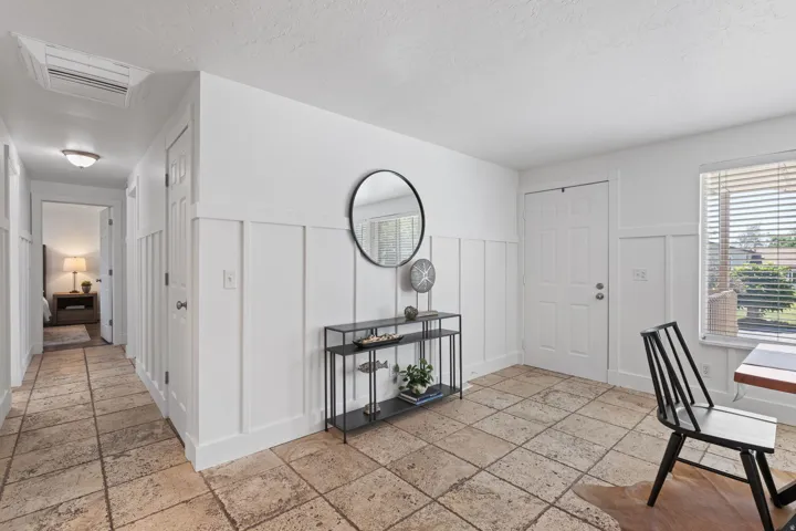Tiled flooring extending throughout, crisp white board and batten wall detailing, a paneled entry door, and a single window with horizontal blinds