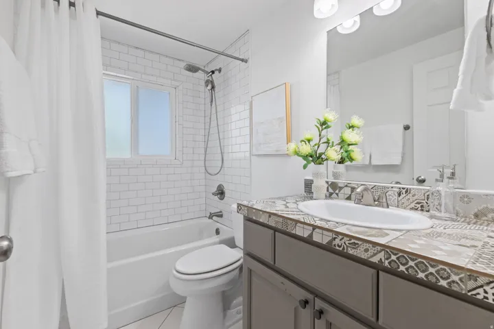 Subway tile bath surround with a window, a single vanity with a patterned tile countertop, and a built-in mirror with overhead lighting