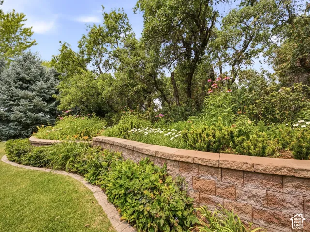 Curved retaining wall with layered plantings, mature trees, and a manicured lawn