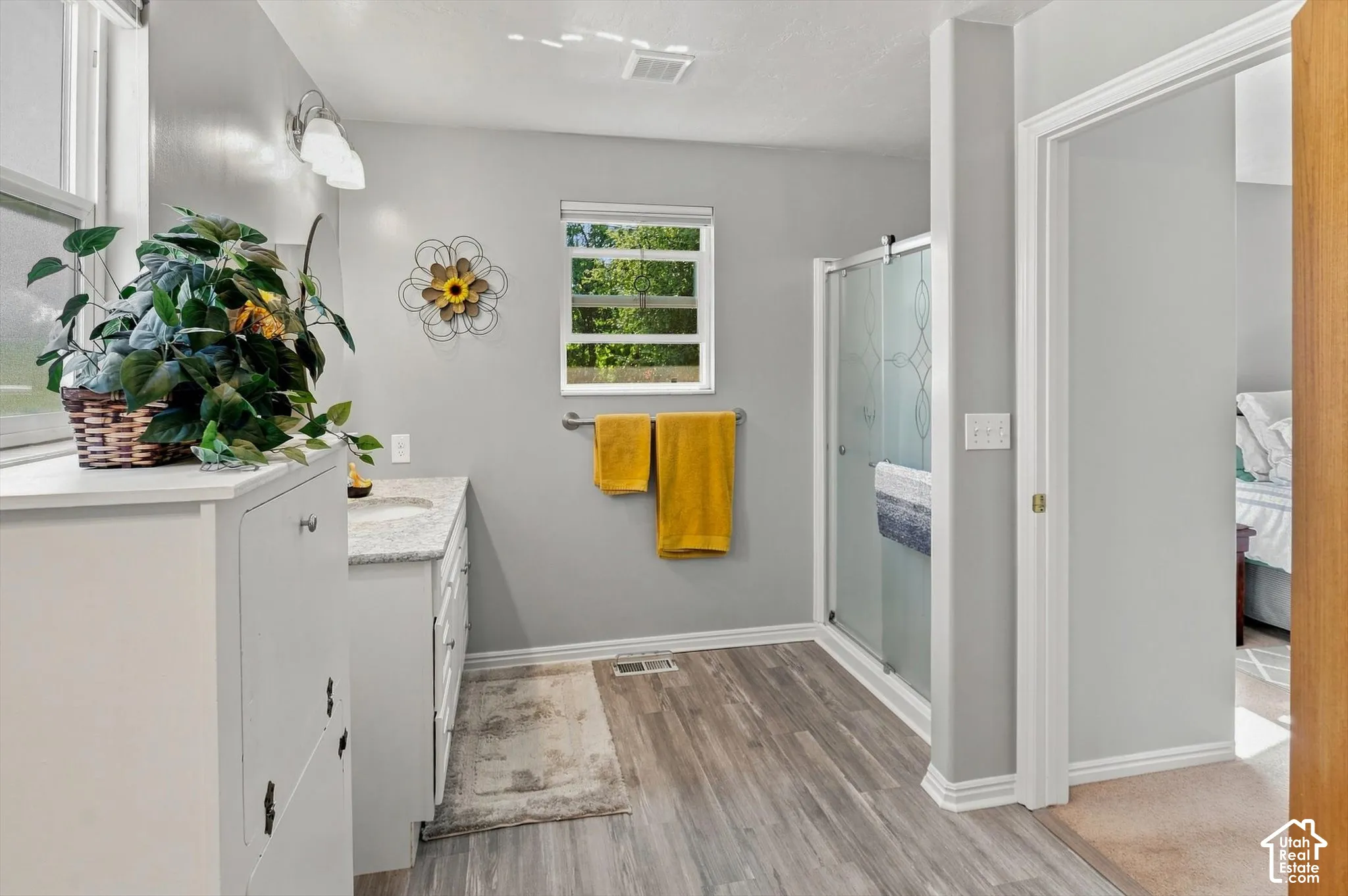 Bathroom featuring a single vanity with stone countertop, wood-finish flooring, a glass-enclosed shower, and a window with natural light